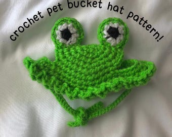 May include: Green crocheted frog bucket hat with white eyes for a pet. The hat has a ruffle trim and a long tie.