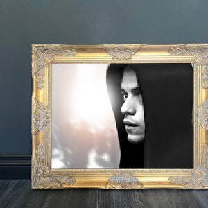 May include: A black and white photo of a person wearing a hooded sweatshirt, framed in a gold ornate frame.