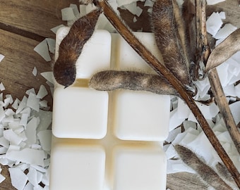 May include: A white wax melt with four squares, surrounded by white coconut flakes and brown soy beans.