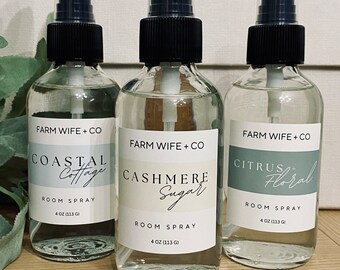 May include: Three glass bottles with black spray tops and white labels. The labels have the text "FARM WIFE + CO" and the names of different scents: "COASTAL Cottage", "CASHMERE Sugar", and "CITRUS Floral". Each bottle contains 4 oz (113 g) of room spray.