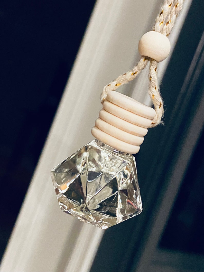 May include: A clear glass diamond-shaped bottle with a wooden cap and a white string with a wooden bead. The bottle is hanging from the string.