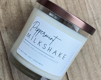 May include: A white candle in a clear glass jar with a brown lid. The label reads "Peppermint Milkshake" and lists the scent notes as "Fresh Mint | Vanilla | Sugar Milk | Chocolate". The candle is made with all-natural soy wax and weighs 8.5 ounces (241 grams).
