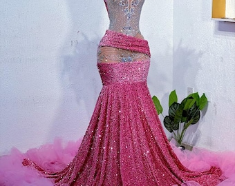 May include: A pink sequined gown with a sheer bodice and a large pink tulle train. The gown is decorated with silver embellishments and feathers.