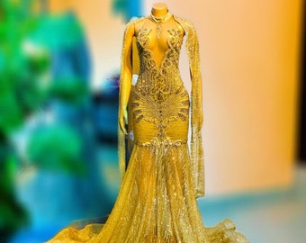 Puede incluir: Un vestido de lentejuelas dorado con un escote pronunciado y una larga cola. El vestido tiene un corpiño ajustado y una falda fluida.