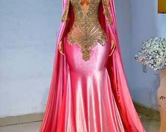 Puede incluir: Un vestido de noche rosa y dorado con una larga cola y un corpiño ajustado. El corpiño está adornado con lentejuelas y cuentas doradas. El vestido está hecho de una tela suave y fluida.