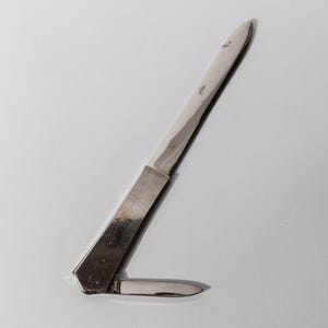May include: A small, silver pocket knife with two blades. One blade is extended, and the other is folded into the handle. The knife is set against a white background.