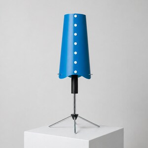 Könnte beinhalten: Eine leuchtend blaue Tischlampe mit einem konischen Schirm, der mit weißen kreisförmigen Akzenten verziert ist. Die Lampe hat einen schwarzen Stiel und ein Stativ, alles vor weißem Hintergrund.