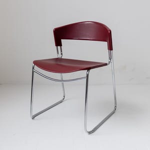 May include: A burgundy-colored chair with a curved back and seat. The chair has a chrome-colored metal frame. The chair is a modern design and is suitable for use in a dining room or office setting.
