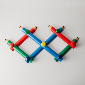 Könnte beinhalten: Ein bunter, bleistiftförmiger Kleiderständer mit blauen, roten und grünen Bleistiften. Jeder Bleistift hat einen andersfarbigen Knopf am Ende.