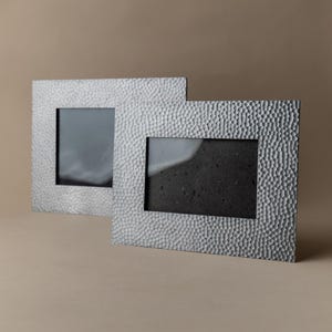 Könnte beinhalten: Zwei silberfarbene Bilderrahmen mit strukturierter, gehammerter Metalloberfläche. Jeder Rahmen hat eine rechteckige Öffnung für ein Foto. Die Rahmen werden vor einem neutralen Hintergrund präsentiert.