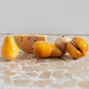 Puede incluir: Un conjunto de cinco esculturas de frutas talladas a mano en mármol amarillo y blanco. El conjunto incluye una sandía, una pera, una manzana y dos mangos.