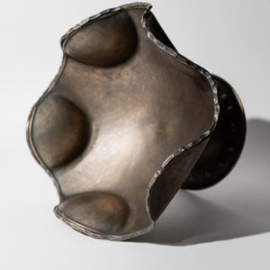 May include: A handcrafted, metallic bronze-colored bracelet with a unique, undulating design. The bracelet features a textured, hammered edge and three raised, rounded elements. The overall shape is organic and sculptural, suitable for artistic jewelry.