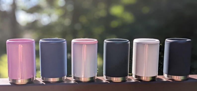 Puede incluir: Siete enfriadores de latas aislados en varios colores, incluyendo rosa, azul, blanco y negro. Los enfriadores est&aacute;n hechos de acero inoxidable y tienen un dise&ntilde;o de doble pared para mantener las bebidas fr&iacute;as.