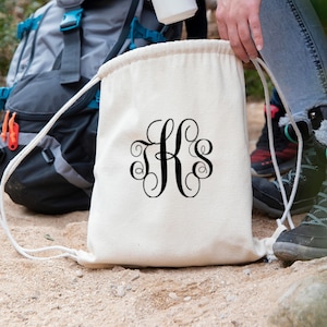 May include: A white drawstring bag with black  "KS" monogram in a script font.