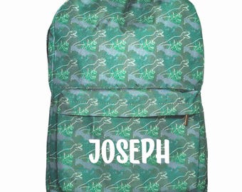 May include: A green backpack featuring a repeating pattern of white dinosaur outlines. The front pocket displays the name JOSEPH in bold, white, sans-serif capital letters. The bag has a main compartment and a smaller front zippered pocket.