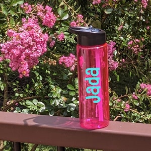 May include: A pink water bottle with a black lid and a turquoise name "Jada" on the side.