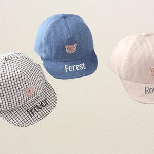 May include: Three children's baseball caps with embroidered bear faces and personalized names. The caps are in blue denim, black and white checkered, and beige.
