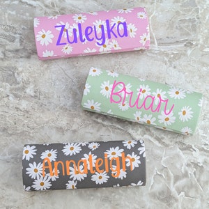 May include: Three floral patterned eyeglass cases with personalized names: Zuleyka, Briar, and Annaleigh. The cases are pink, green, and gray.