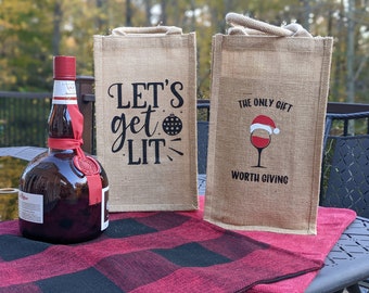 May include: Two brown burlap gift bags with festive Christmas designs. The bag on the left says "Let's get lit" with a disco ball ornament. The bag on the right says "The only gift worth giving" with a glass of wine with a Santa hat on top.