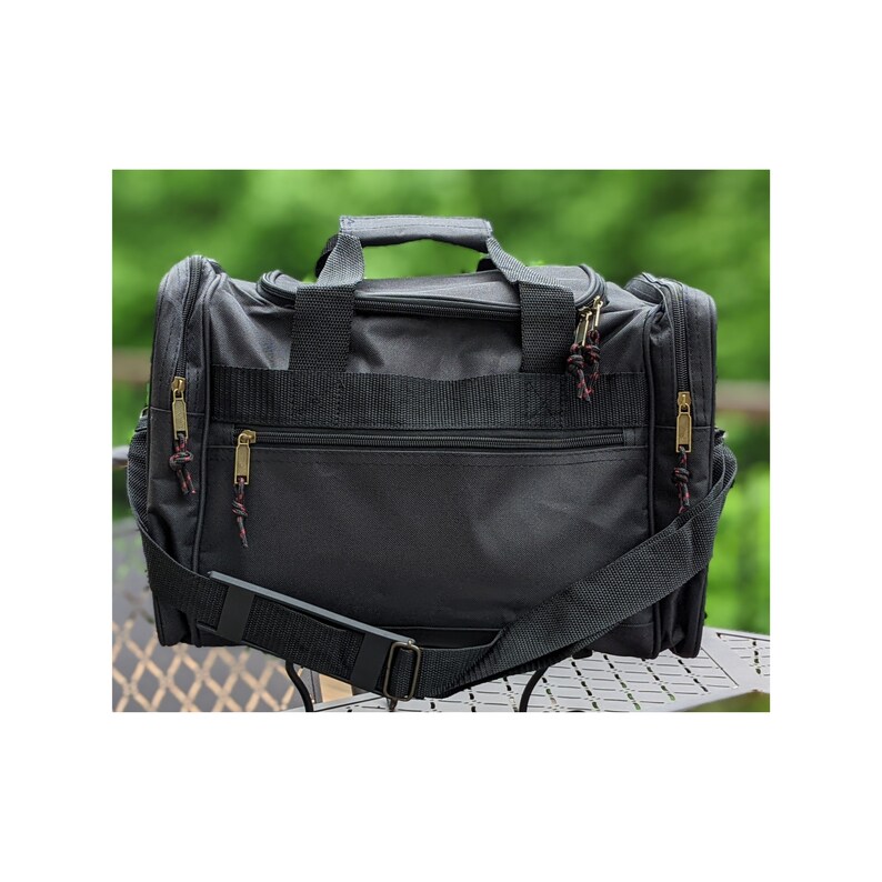 K&ouml;nnte beinhalten: Schwarze Reisetasche mit einem Rei&szlig;verschluss-Hauptfach und einem Schultergurt. Die Tasche hat zwei Rei&szlig;verschlussf&auml;cher an der Vorderseite und zwei Rei&szlig;verschlussf&auml;cher an den Seiten.