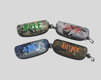 May include: Four camouflage patterned eyeglass cases with personalised names: Kyle, Archie, Amy, and Bryce. Each case has a zipper and a metal loop.