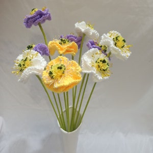 May include: A bouquet of crocheted flowers in a white vase. The flowers are white, yellow, and purple.