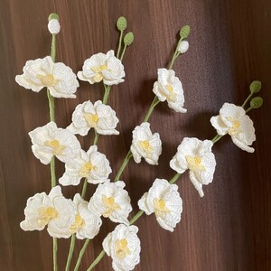 Może przedstawiać: Bukiet białych kwiatów orchidei wykonanych na szydełku z żółtymi środkami i zielonymi łodygami.