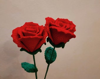 May include: Two crocheted red roses with green leaves and stems.