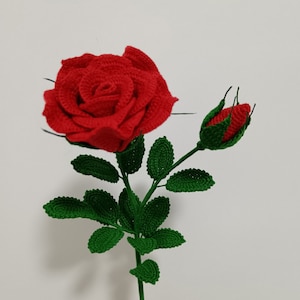 Può includere: Una rosa rossa all'uncinetto con foglie verdi e un bocciolo.