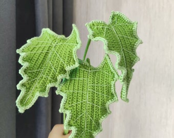 May include: A crocheted green plant with three leaves. The leaves have a light green outline and are textured.