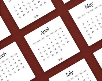 May include: A collection of white 2026 monthly calendars arranged on a dark red surface. Each calendar displays the month's name and dates in a simple, readable font. The calendars are slightly angled, creating a dynamic composition.