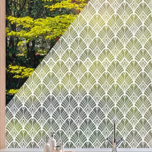 Könnte beinhalten: Ein Fenster mit einem weißen Art-Deco-Muster-Overlay. Das Muster ist ein sich wiederholendes Fächerdesign. Das Fenster zeigt einen Blick auf grünes Laub und einen Holzrahmen. Das Fenster befindet sich in einer Küche mit Seifenspendern und einem Wasserhahn.