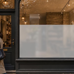 May include: A shopfront window featuring a large, rectangular section of semi-transparent frosted privacy film applied to the glass. The film creates a matte, opaque surface that obscures the view into the interior whilst allowing light to pass.
