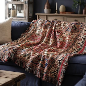 May include: A decorative throw blanket with a detailed floral pattern in red, cream, blue, and green, draped over a navy blue sofa. The blanket has a fringed edge and a traditional design, adding a touch of elegance to the living room.
