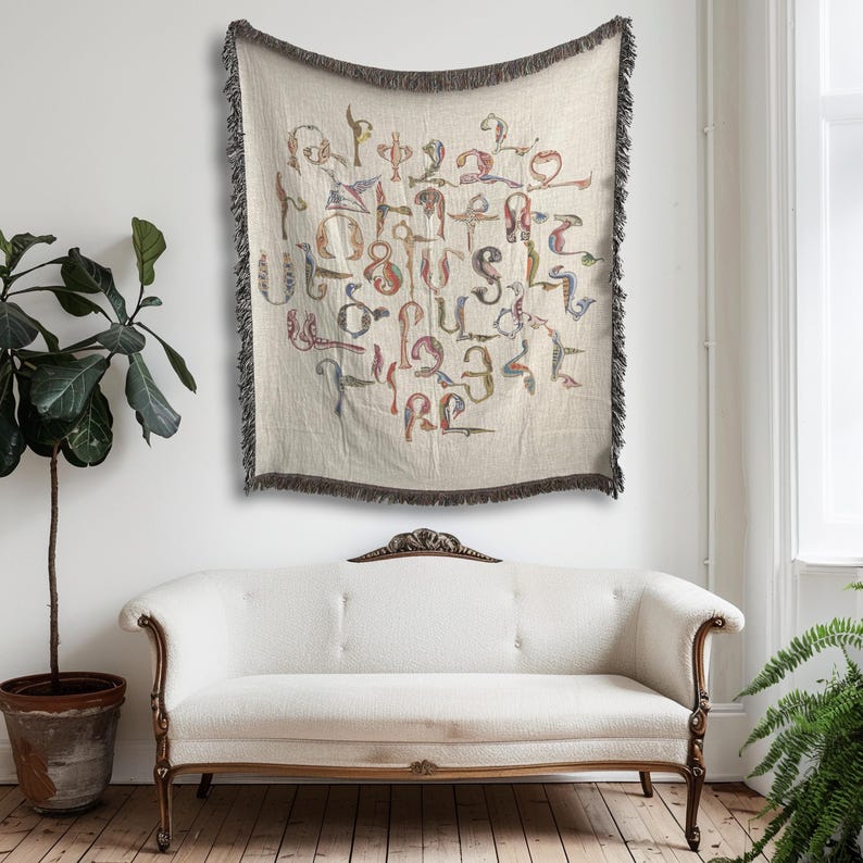 Cream Armenian bird-letter blanket used as a wall hanging above a pale armchair beside a leafy plant.