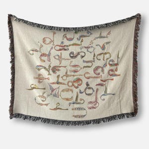 Cream Armenian bird-letter woven blanket hanging against a white wall, with a curved lower edge and dark fringe.