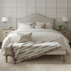 Turquoise, rust and cream patterned fringed blanket folded across the foot of a bed with neutral pillows in a bright bedroom.
