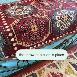 a colorful, intricately patterned rug or carpet placed on a metal frame, with a caption that reads "the throw at a client's place".