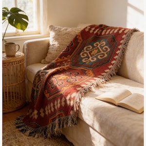 a cozy living room scene with a vibrant, patterned throw blanket draped over a beige sofa, an open book on the armrest, and a potted plant nearby.