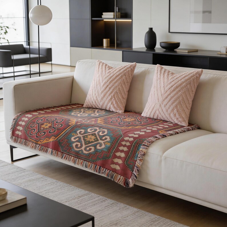 a modern living room with a white sofa adorned with a colorful patterned throw blanket and two matching throw pillows. The room features a black coffee table, a bookshelf, and a window, creating a cozy and inviting atmosphere.