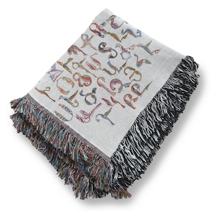 Folded cream Armenian bird-letter blanket on a white background, showing multicolored lettering and dark woven fringe.