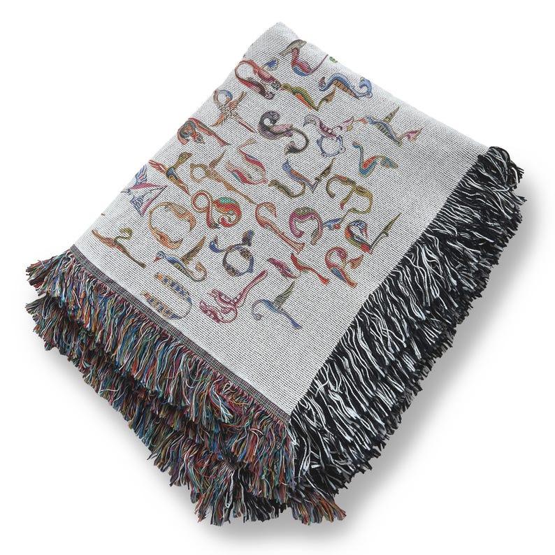 Folded cream Armenian bird-letter blanket on a white background, showing multicolored lettering and dark woven fringe.