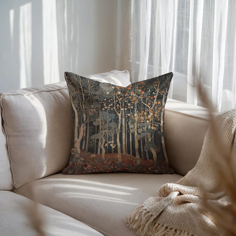 A decorative throw pillow with a forest scene sits on a beige couch, with a white blanket draped over the armrest.