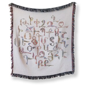Full vertical view of a cream woven blanket with colorful Armenian bird-shaped letters and dark fringe against a light background.