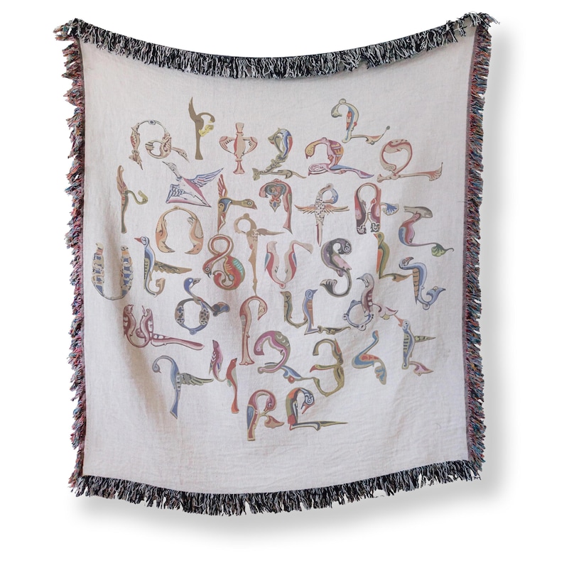 Full vertical view of a cream woven blanket with colorful Armenian bird-shaped letters and dark fringe against a light background.