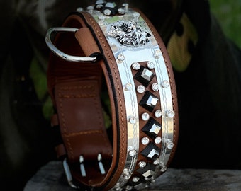 Puede incluir: Un collar de perro de cuero marrón con detalles plateados y pedrería. El collar tiene un dije de cabeza de lobo plateado.