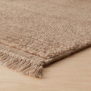Könnte beinhalten: Nahaufnahme eines beigefarbenen Teppichs mit strukturierter Oberfläche und Fransen. Der Teppich besteht aus einem weichen Material und hat eine neutrale Farbpalette. Der Teppich eignet sich für die Heimdekoration.