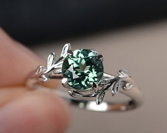 May include: A silver ring with a green gemstone set in a leafy design.