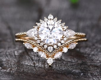 May include: A gold engagement ring set with a large round center stone surrounded by smaller round stones. The band is adorned with pear-shaped stones and a delicate beaded design.