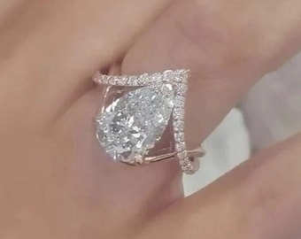 May include: A pear-shaped diamond engagement ring with a rose gold band and a pave setting. The ring features a delicate, V-shaped design on the band.
